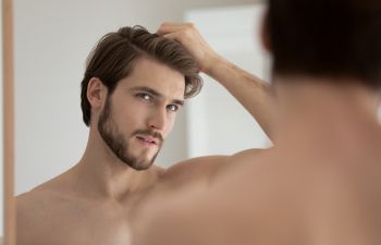 Handsome man combing his hair with fingers in front of a mirror